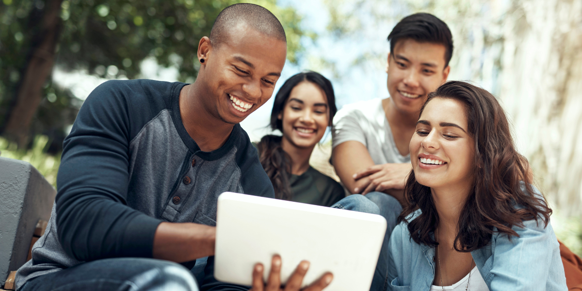 picture of four university students looking at an iPad together smiling